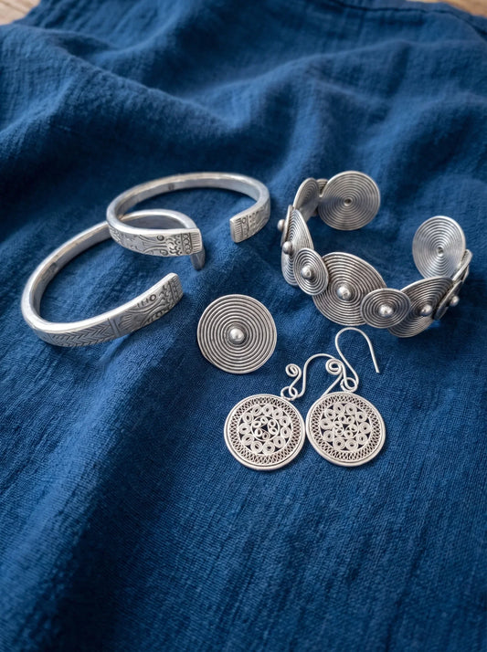 Miao-style silver-colored bracelets, earrings, and disc ornaments arranged on indigo textile