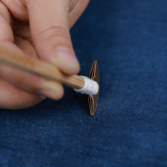 Hand applying a Miao Batik wax knife to a blue background