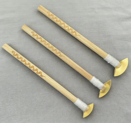Three decorative miao batik tools with gold accents on a gray fabric background