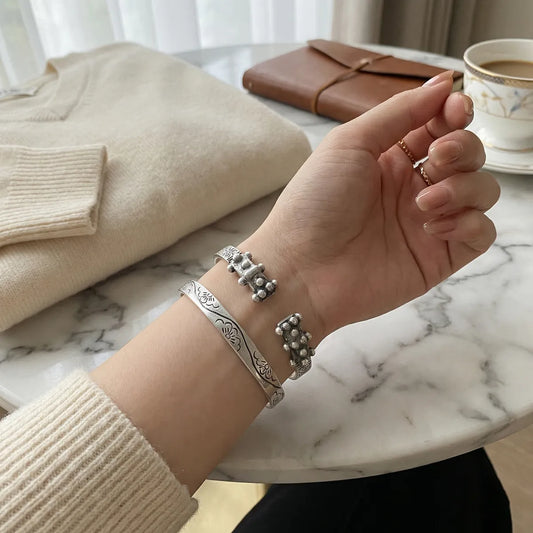 Hand wearing miao silver bracelets on a marble surface with a cup of coffee and beige sweater in the background