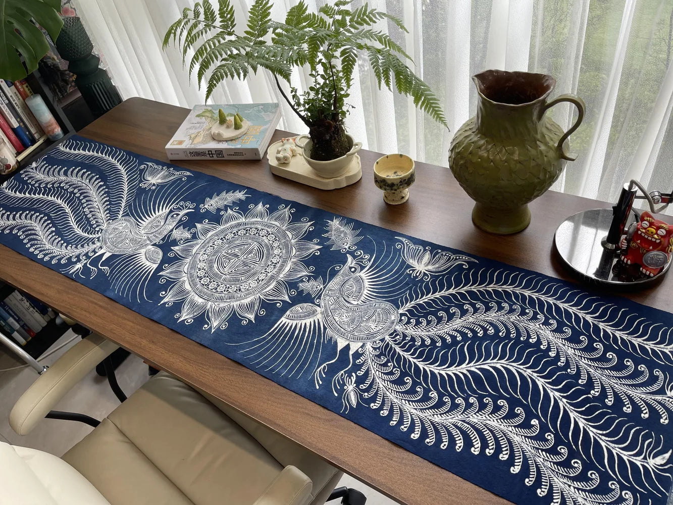 Long handmade Miao batik table runner styled on a wooden table beside a window