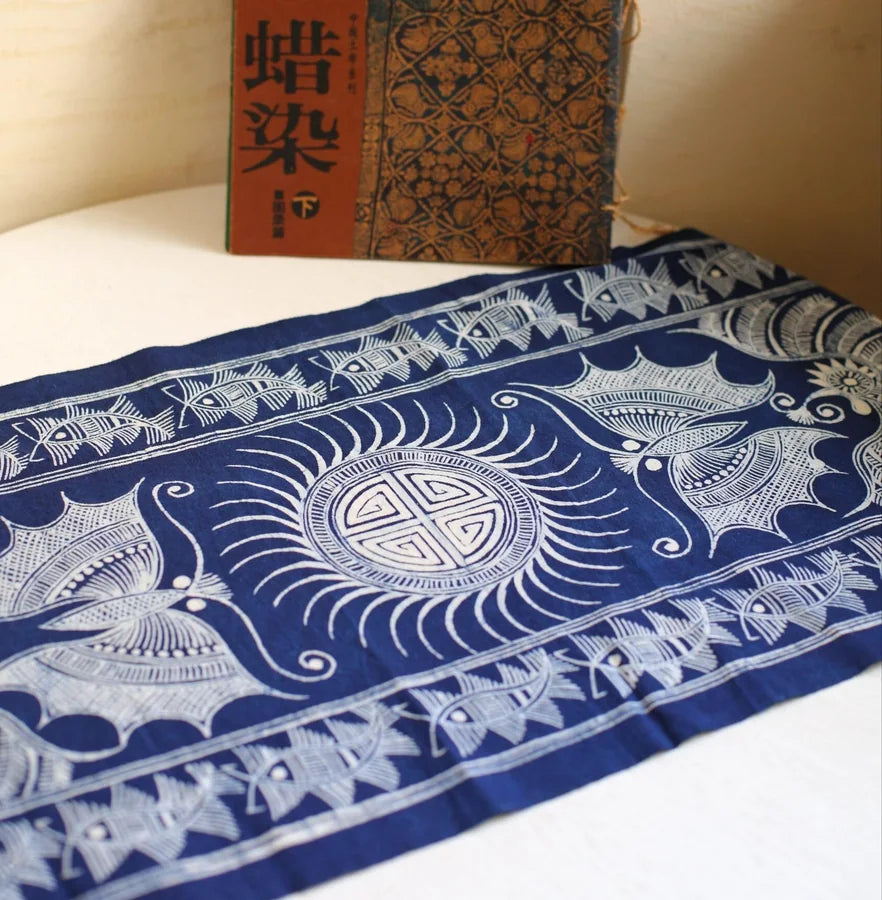 Miao batik textile with birds and a central circular symbol styled on a table