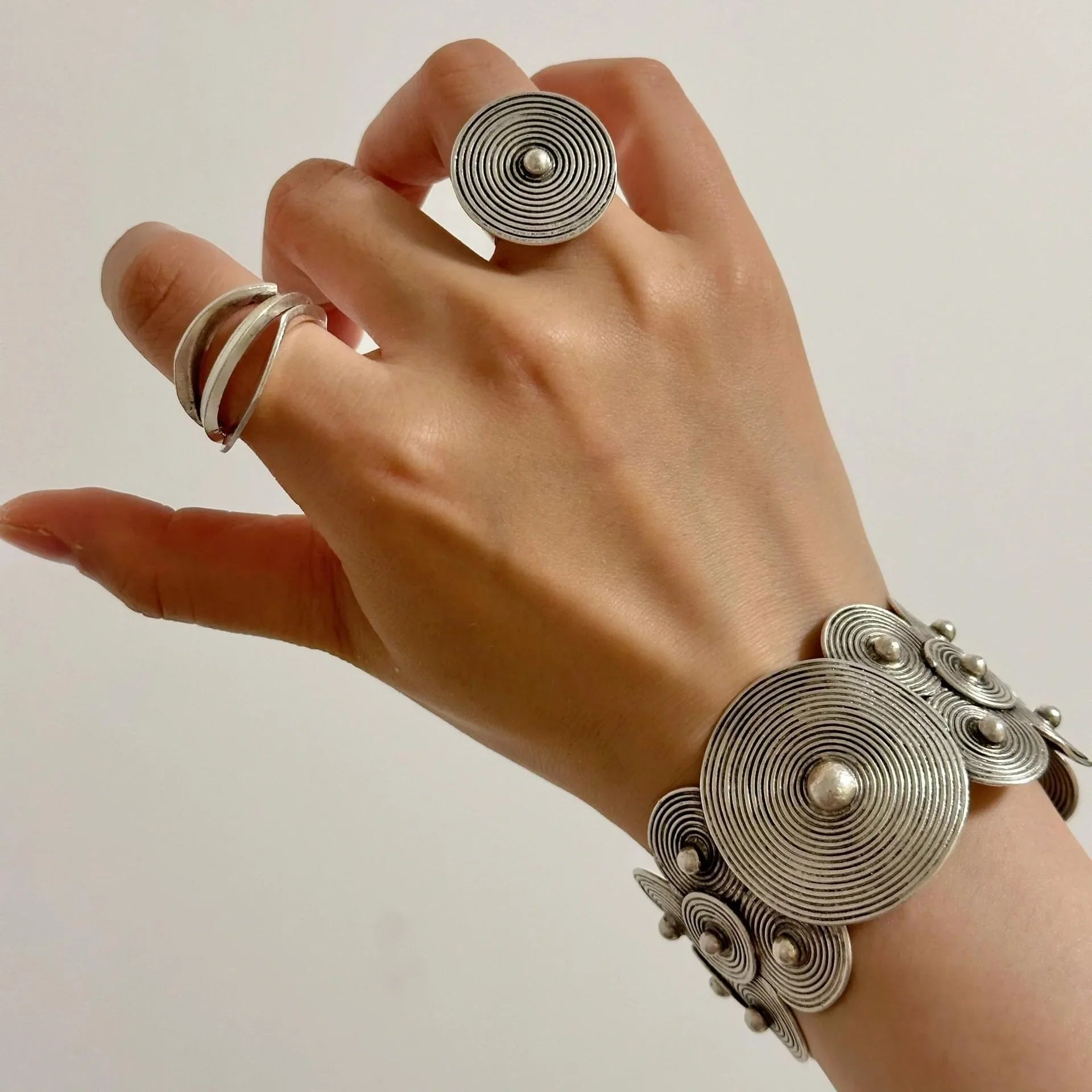 Close detail of a hand wearing a Miao-style silver-colored disc bracelet and ring