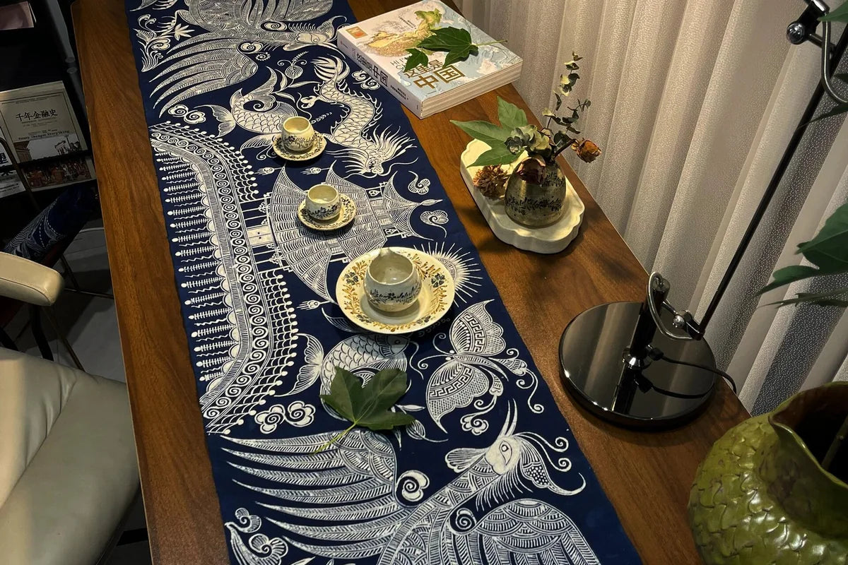 Indigo Miao batik table runner styled across a wooden dining table with tea cups, books and flowers