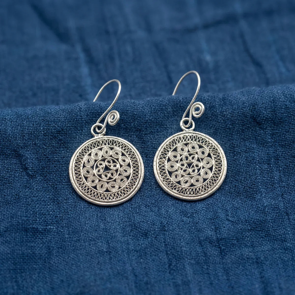 Miao Silver earrings with intricate designs on a blue fabric background