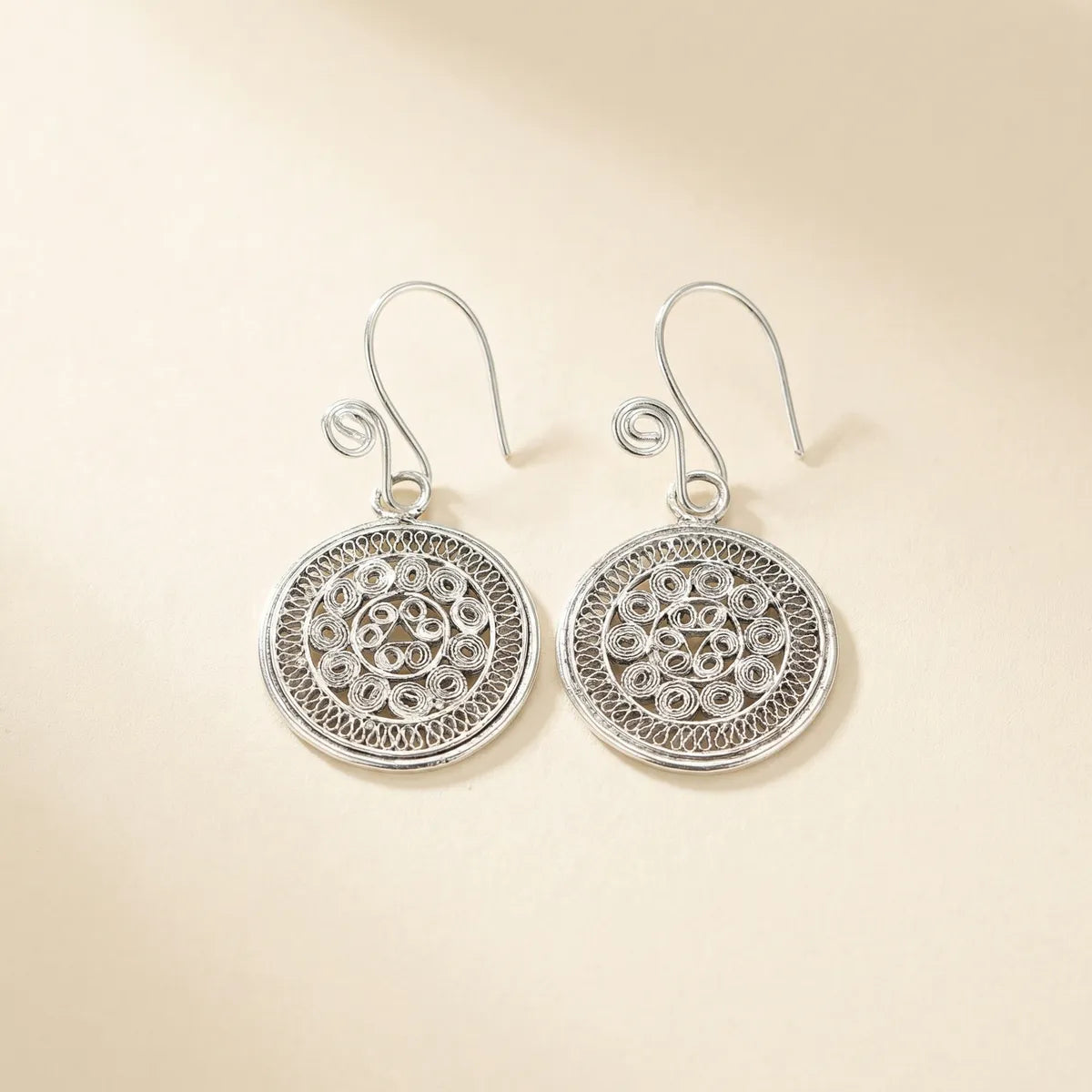 Pair of Miao silver earrings with intricate designs on a beige background
