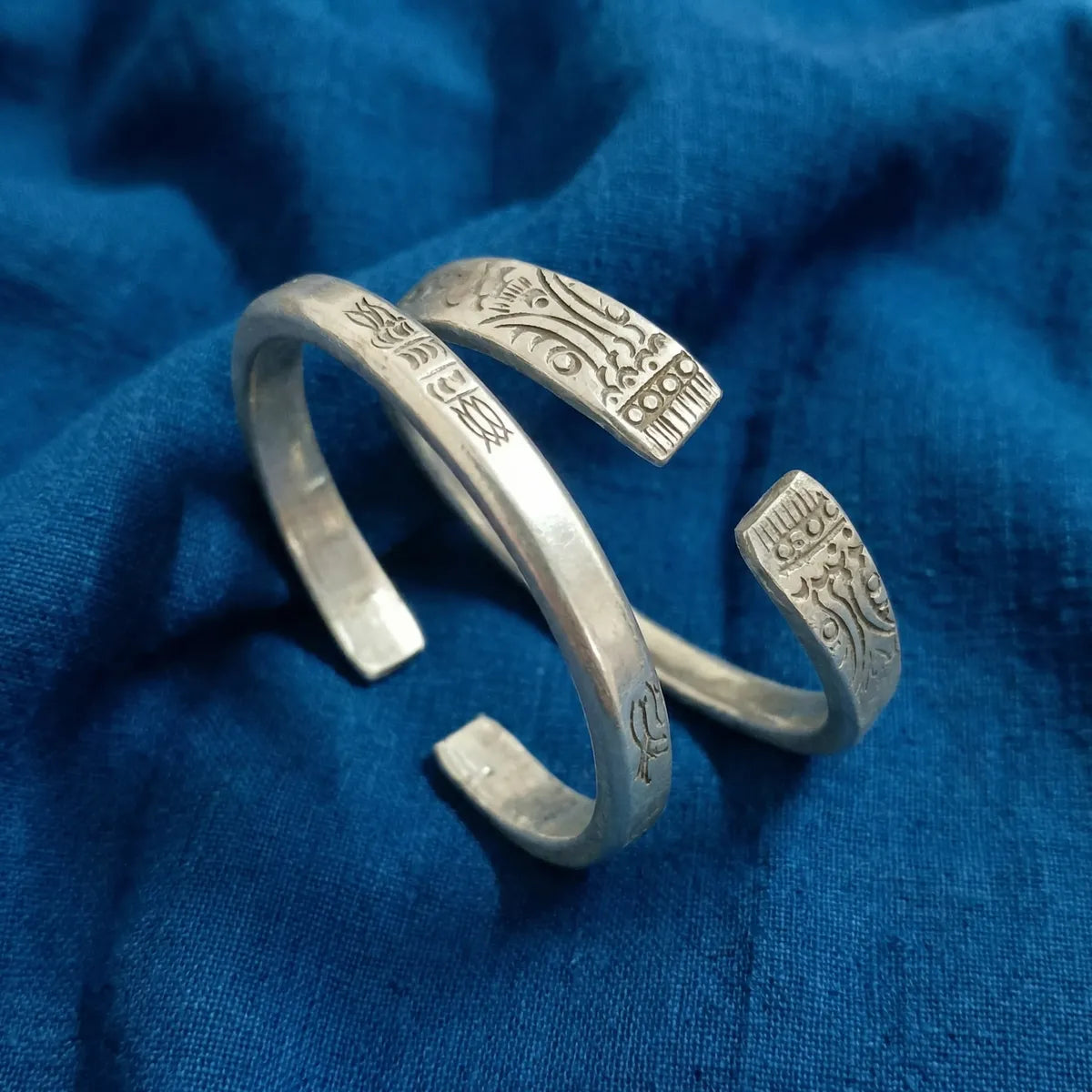 Miao Silver anklets with intricate designs on a blue fabric background