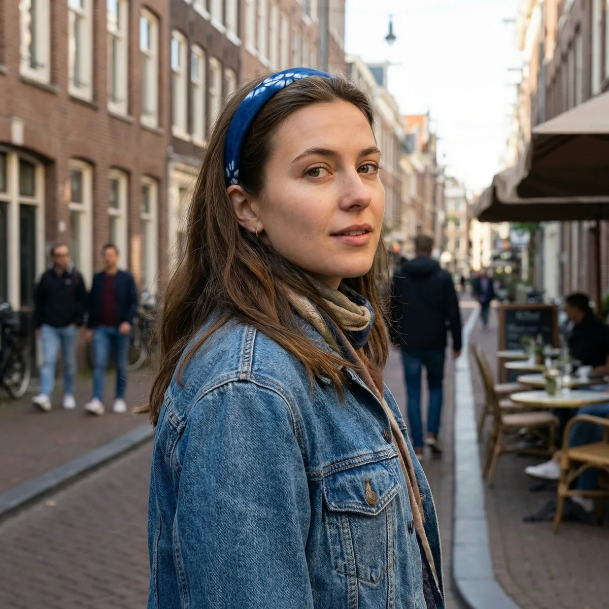Woman wearing a denim jacket and Miao batik headband on a city street.