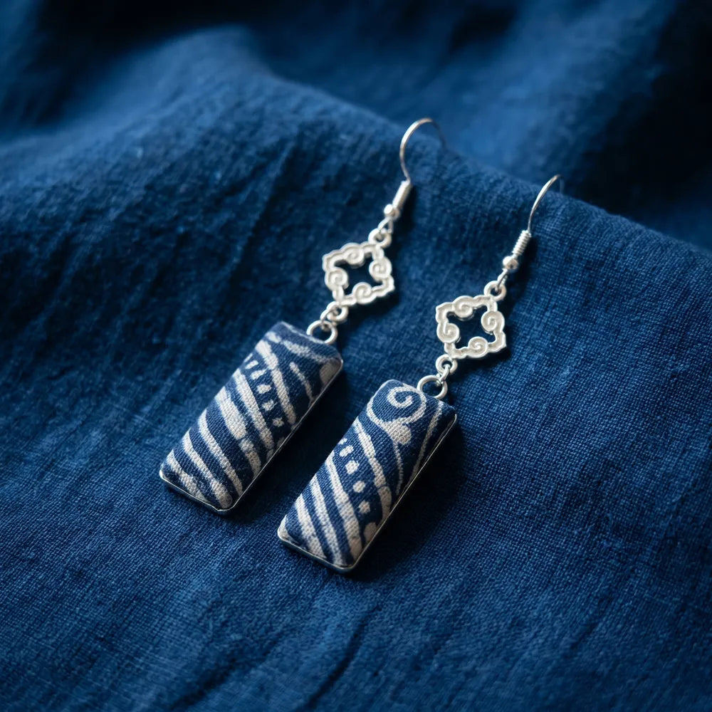 Pair of miao batik earrings with geometric designs on a blue fabric background