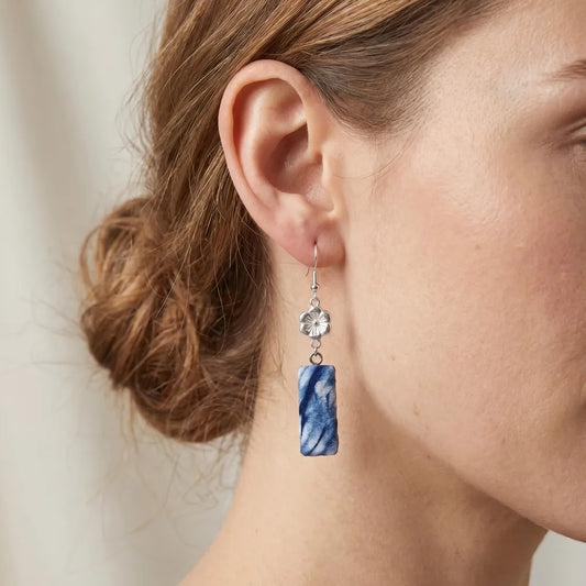 Close-up of a woman wearing a blue marbled earring with a silver flower detail.