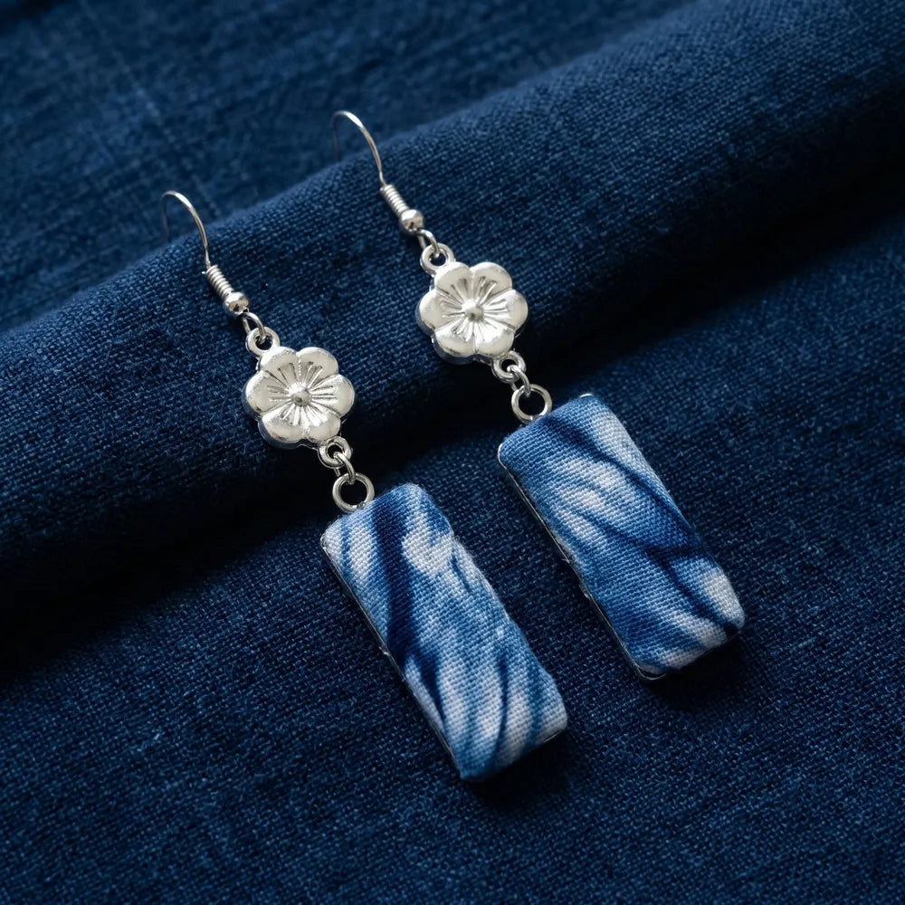 Miao Silver floral earrings with blue rectangular charms on a blue fabric background