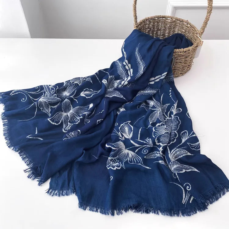 Navy blue Miao batik scarf with white floral patterns draped over a surface with a woven basket in the background.