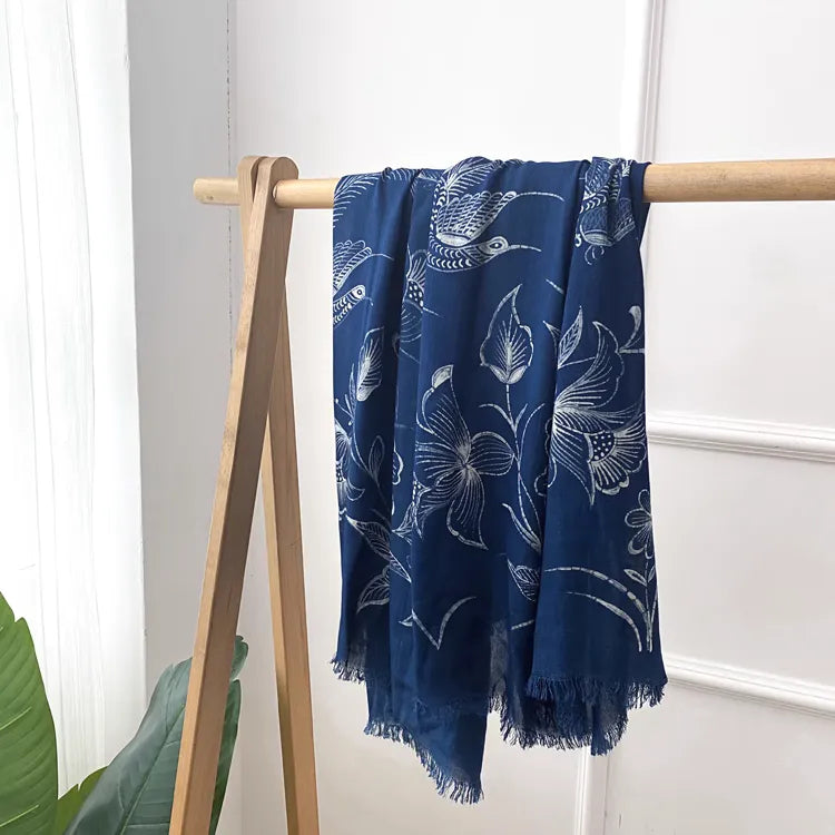 Navy blue Miao batik scarf with white floral patterns draped over a wooden rack against a white wall.