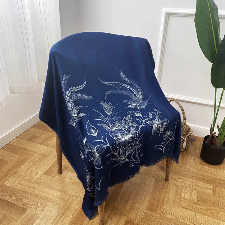 Navy blue Miao batik scarf draped over a chair in a room with wooden flooring and a plant.