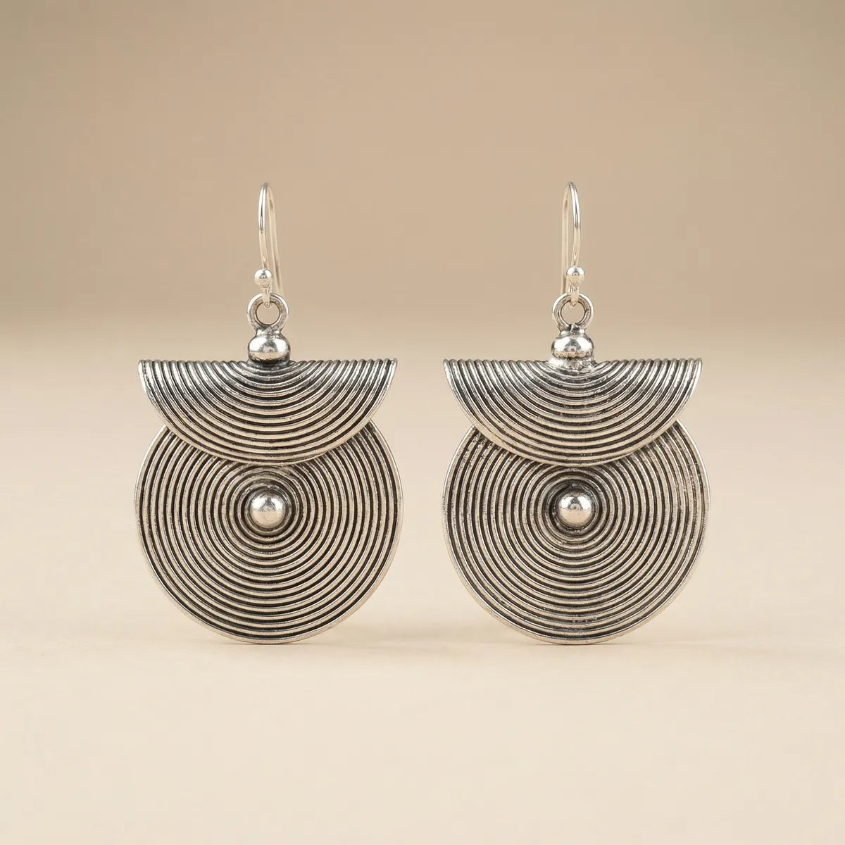 Pair of miao silver earrings with circular designs on a beige background