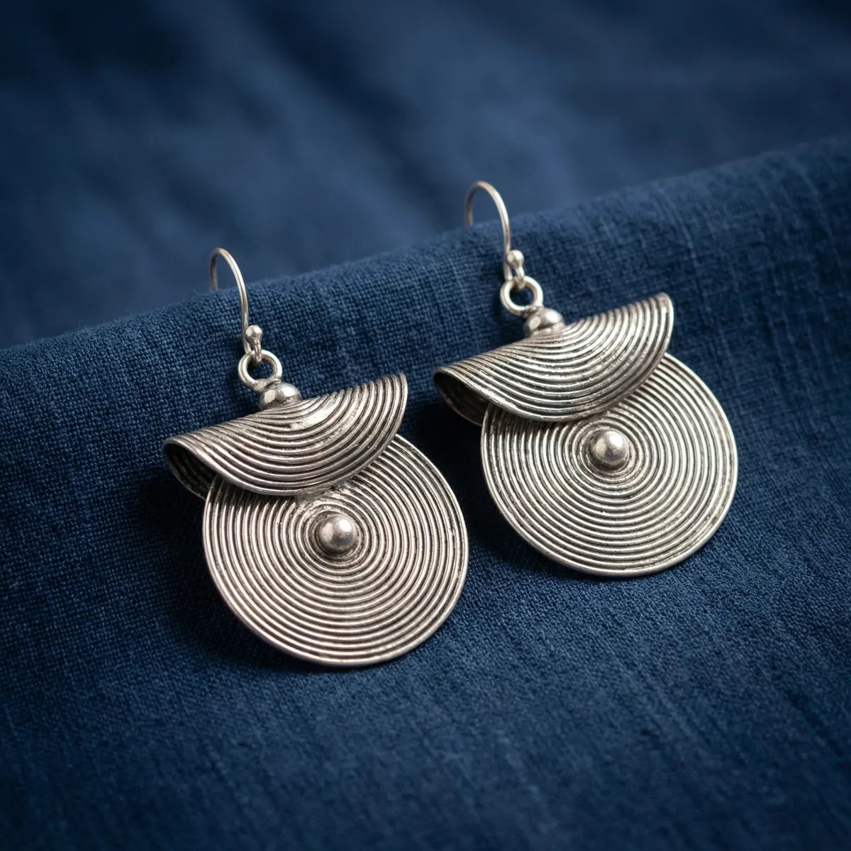 Pair of Miao silver earrings on a blue fabric background