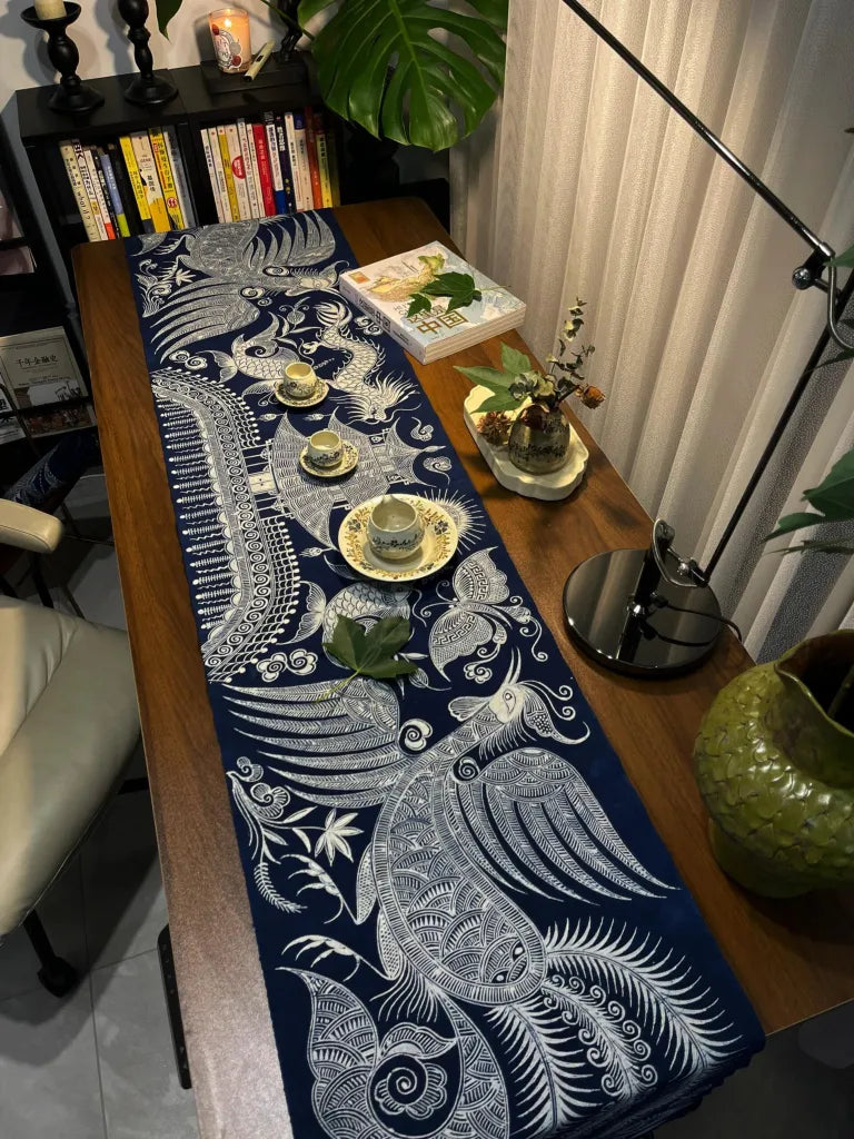 Decorative miao batik table runner with white patterns on a wooden table in a room setting.