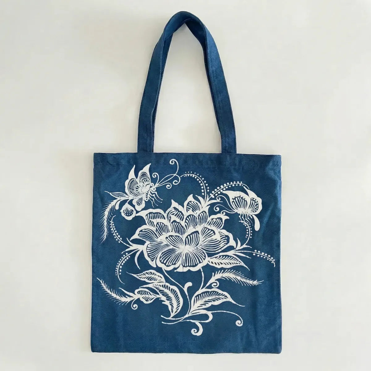 Miao batik tote bag with white floral and butterfly design on a light gray background