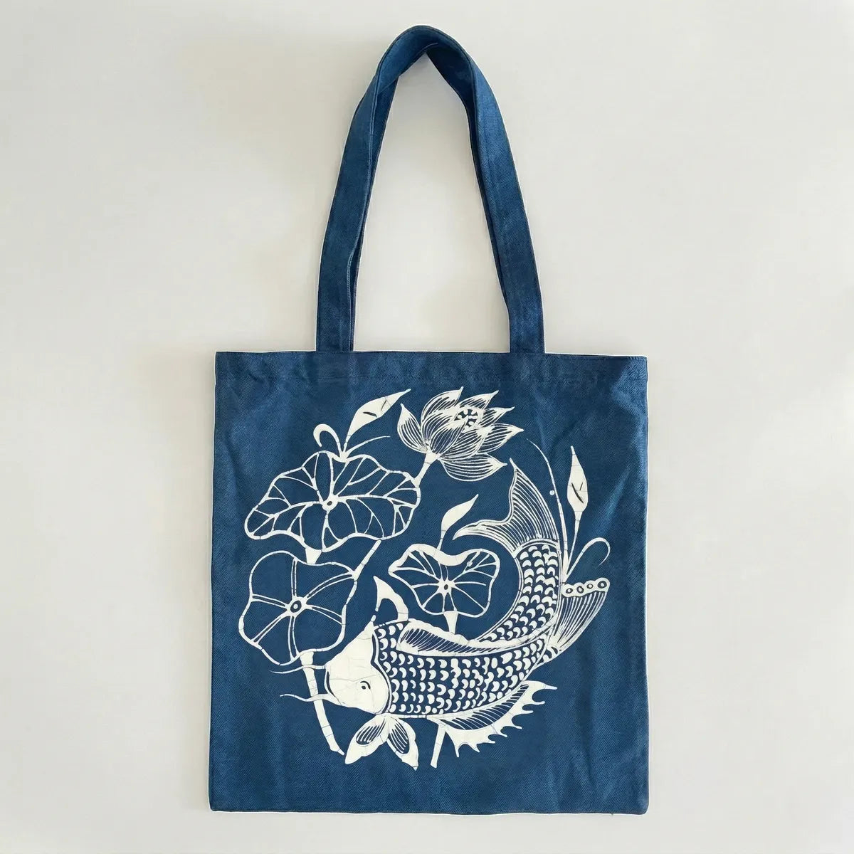 Miao batik tote bag with white floral and fish design on a light gray background
