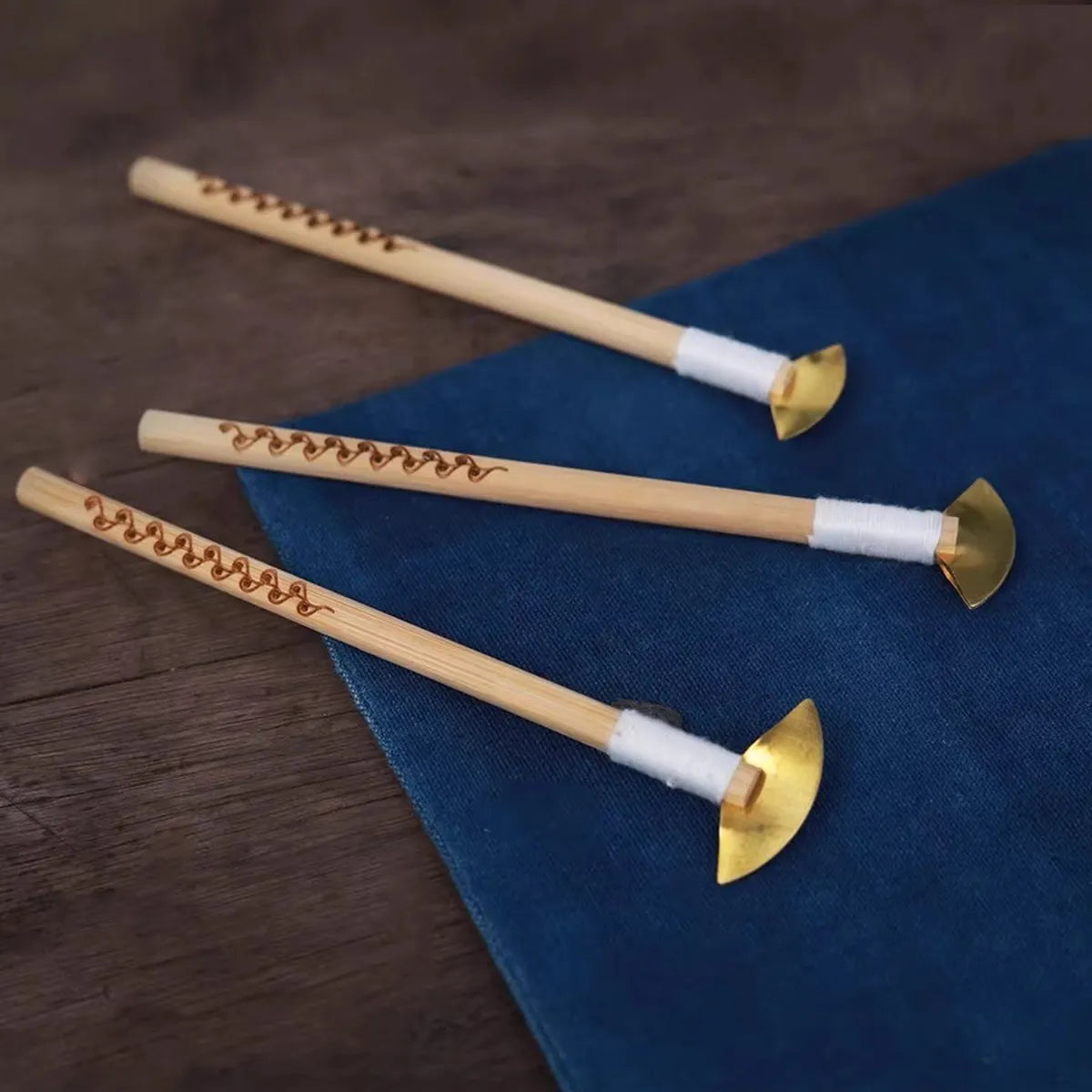 Three wooden Miao Batik wax knife with gold tips on a blue cloth
