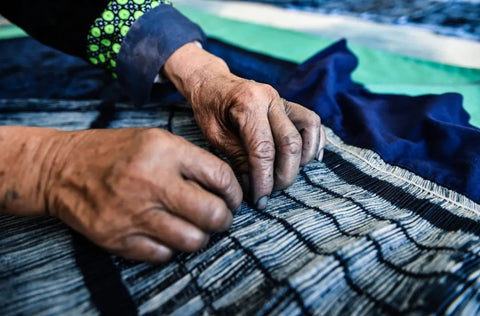 Hands folding a blue Miao batik textile