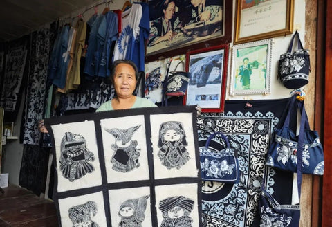 Miao batik artisan standing beside framed indigo textiles
