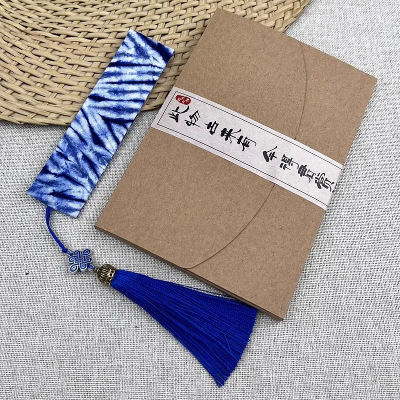 Kraft paper envelope with blue tassel tie-dye bookmark and decorative band on a textured surface