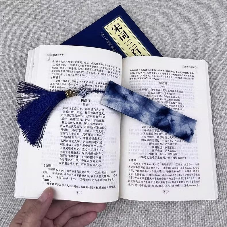 Open book with a blue tassel tie dye bookmark on a gray fabric background