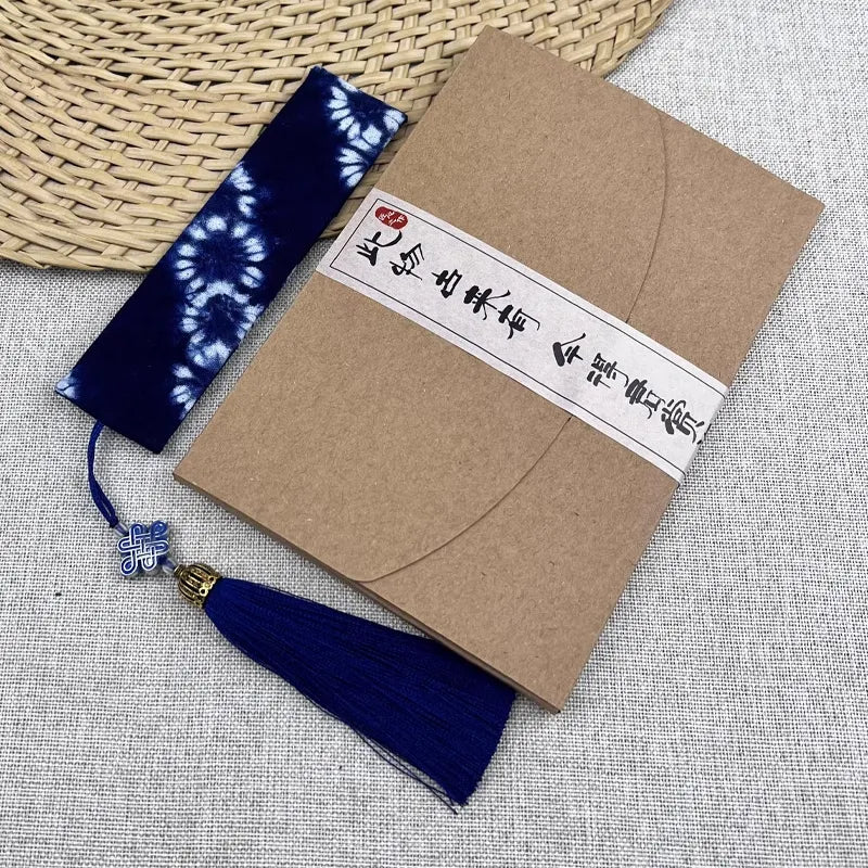 Brown notebook with a blue tassel and decorative tag on a textured surface