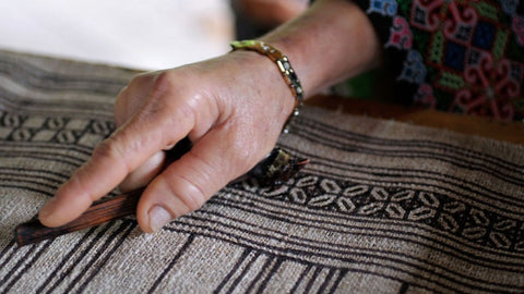 Main suivant une bordure à motifs géométriques sur un tissu de batik Hmong