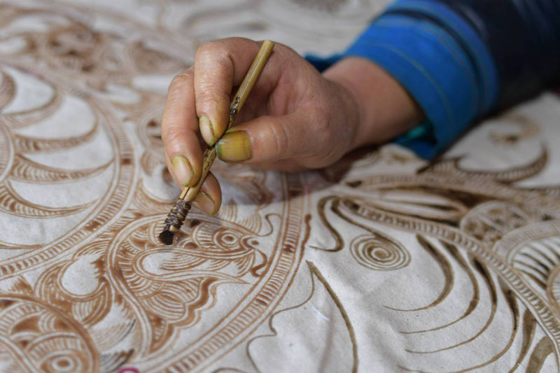 Artisan drawing intricate Miao batik pattern by hand using a wax knife