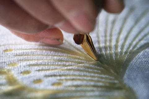 An artisan uses a batik wax tool to draw a fine resist line on fabric