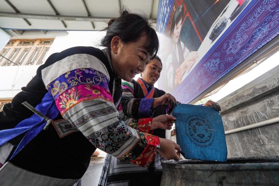 Miao artisan guiding young girls through the indigo dyeing process during a traditional batik workshop.