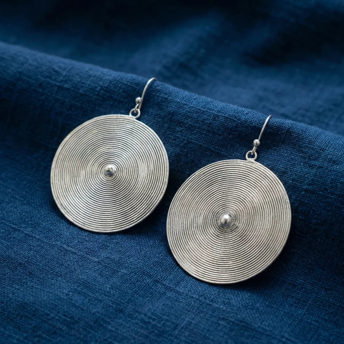 Miao Silver circular earrings on a blue fabric background