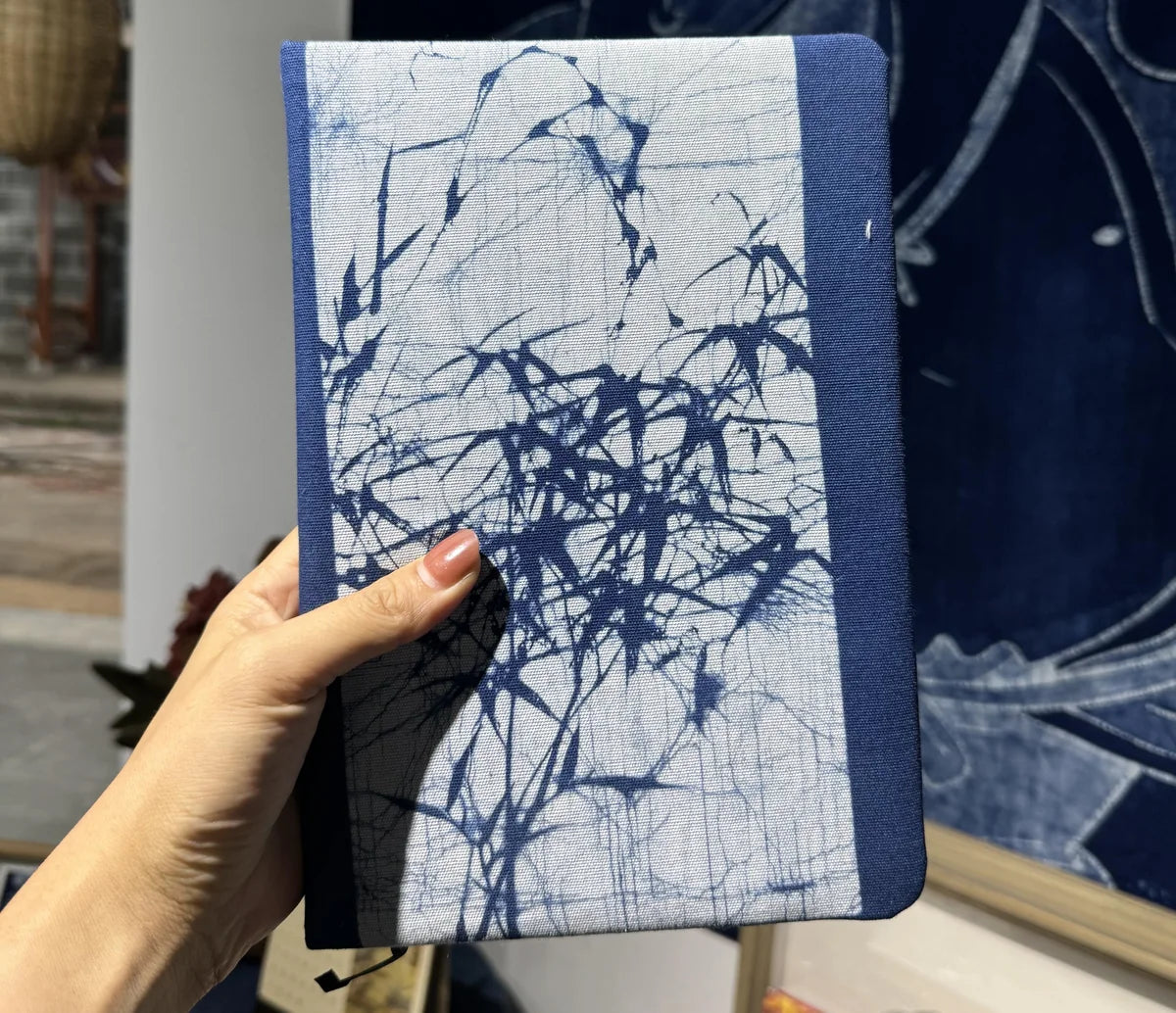 Hand hält ein blau-weißes Batik-Textildetail mit bambusartigen Wachslinien