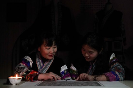 Miao artisans working under warm candlelight in a night-time batik workshop, passing traditional skills to the next generation.