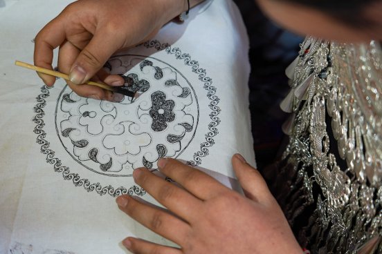 Close-up of a Miao artisan drawing fine wax lines with a traditional wax knife on white cloth.