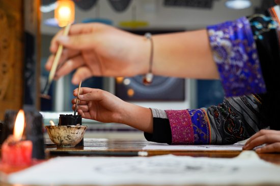 Close-up of a Miao artisan dipping a tool into melted beeswax while preparing to draw wax-resist patterns for batik.