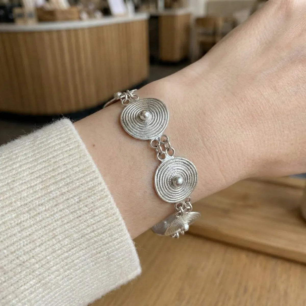 Miao Silver bracelet with circular designs on a wrist, blurred indoor background