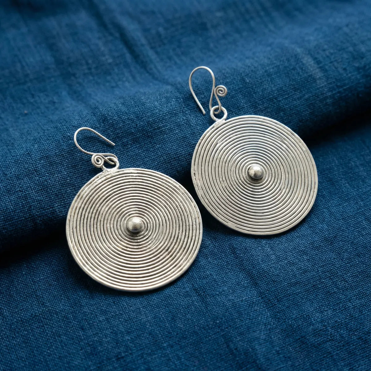 Miao Silver circular earrings on a blue fabric background