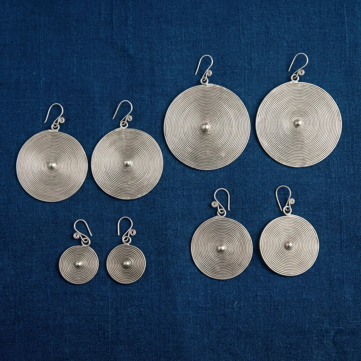 Set of miao silver circular earrings on a blue fabric background