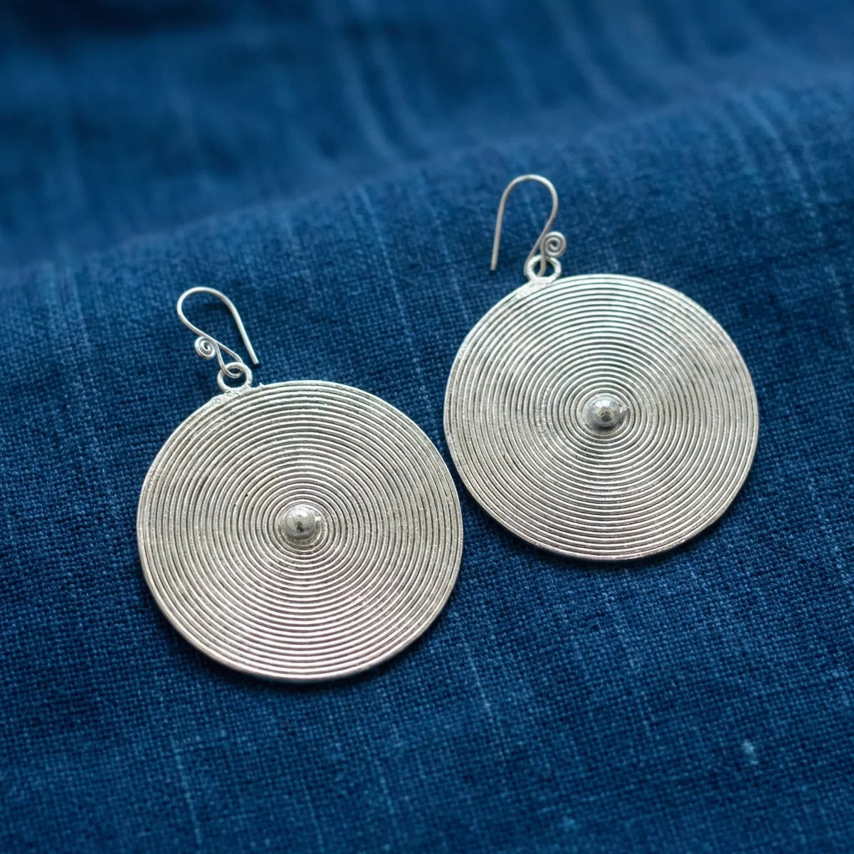 Miao Silver circular earrings on a blue textured fabric background