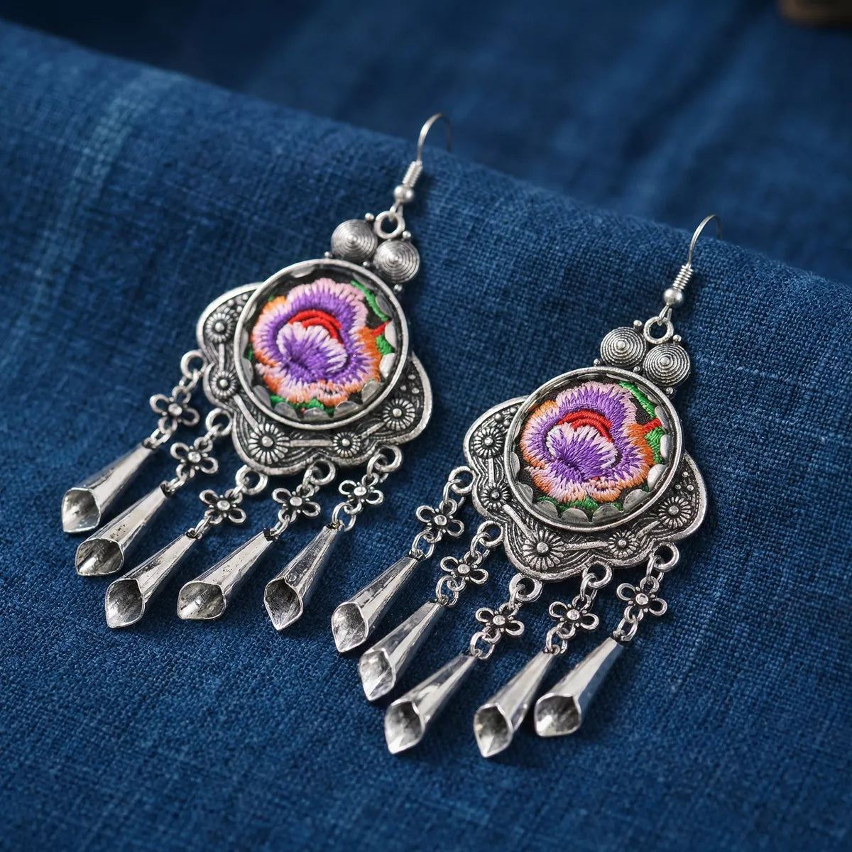 Miao Silver earrings with colorful embroidered stones on a blue fabric background