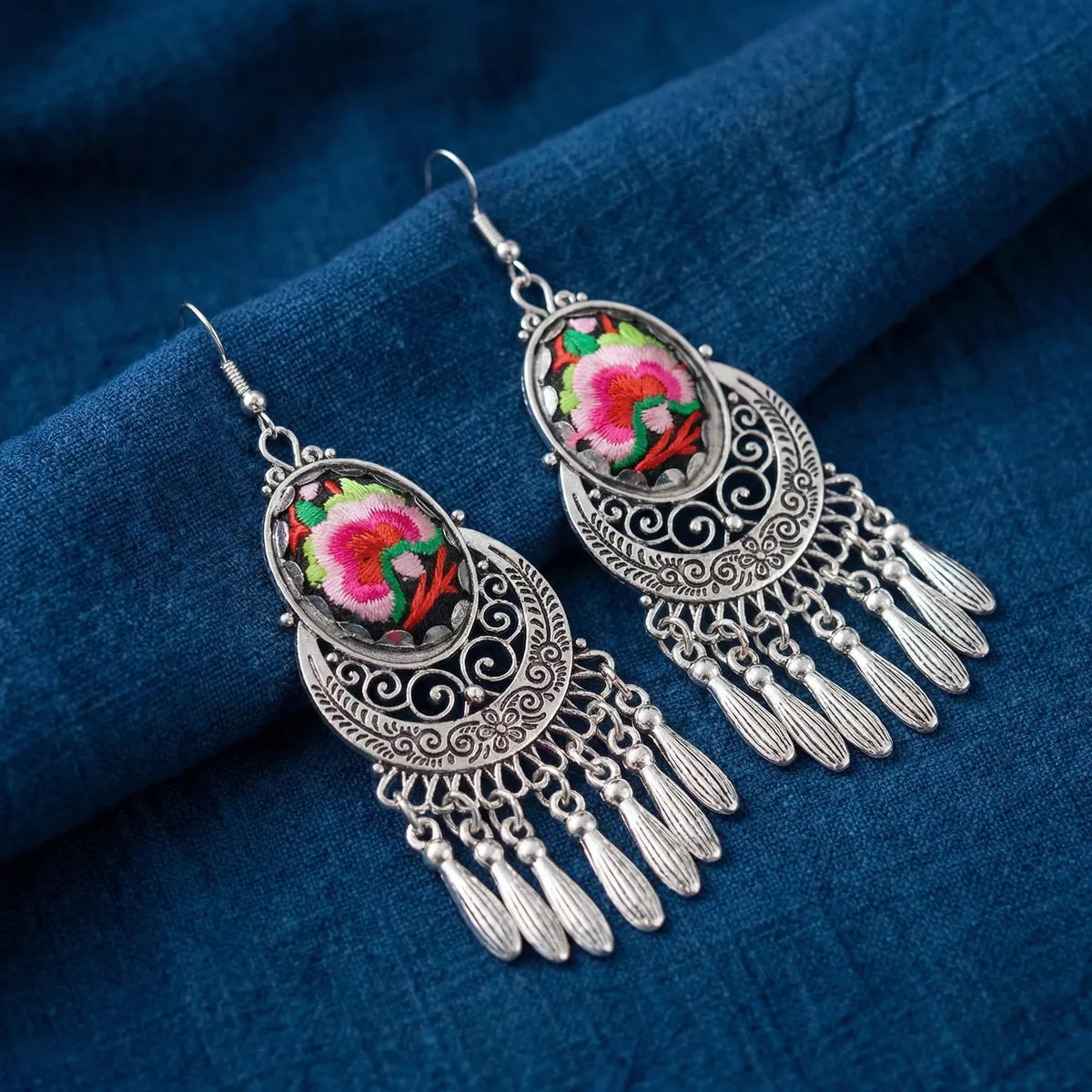 Ornate Miao silver earrings with floral designs on a blue fabric background