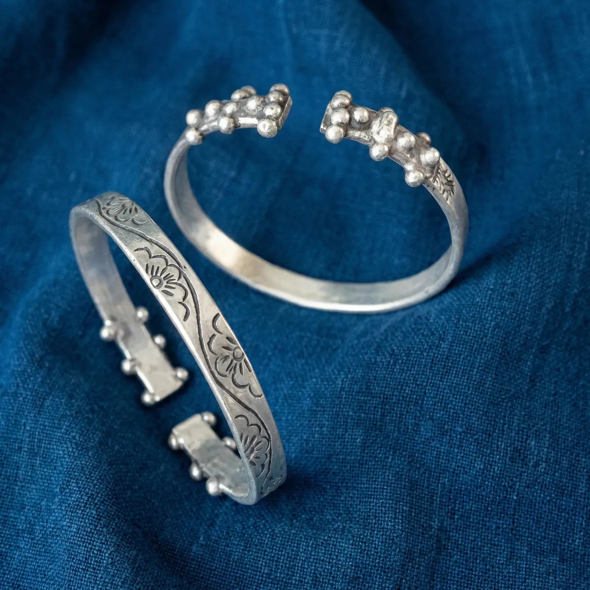 Miao Silver anklets with intricate designs on a blue fabric background