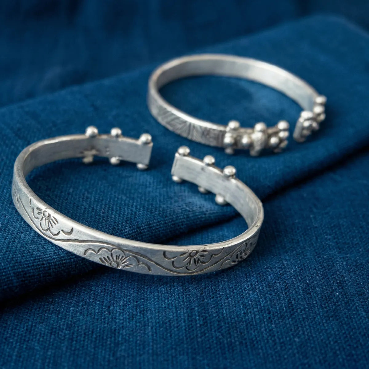 Two Miao silver bracelets with intricate designs on a blue fabric background