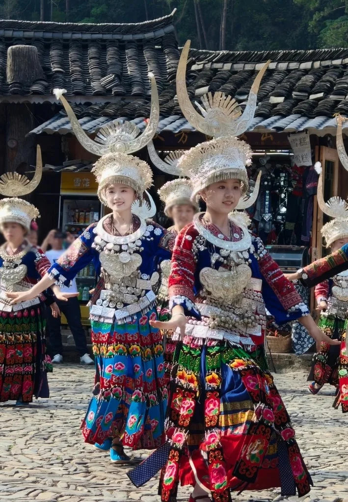 Traditional Miao women performing festival dance in full ceremonial silver headdresses and pleated embroidered attire in Guizhou village