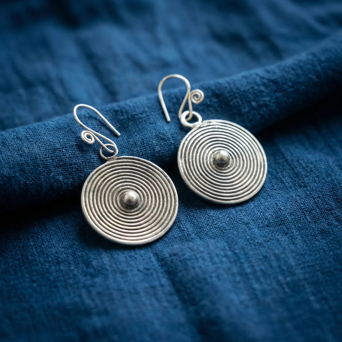 Miao Silver circular earrings on a blue fabric background