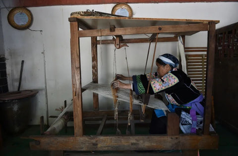Miao artisan working at a wooden loom to weave handmade textile