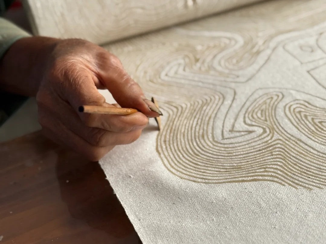 Main dessinant des lignes à la cire sur un tissu avec un couteau à batik